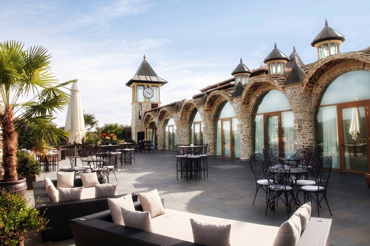 Terraza de una finca con mesas de forja y arcos de piedra, sin decorar